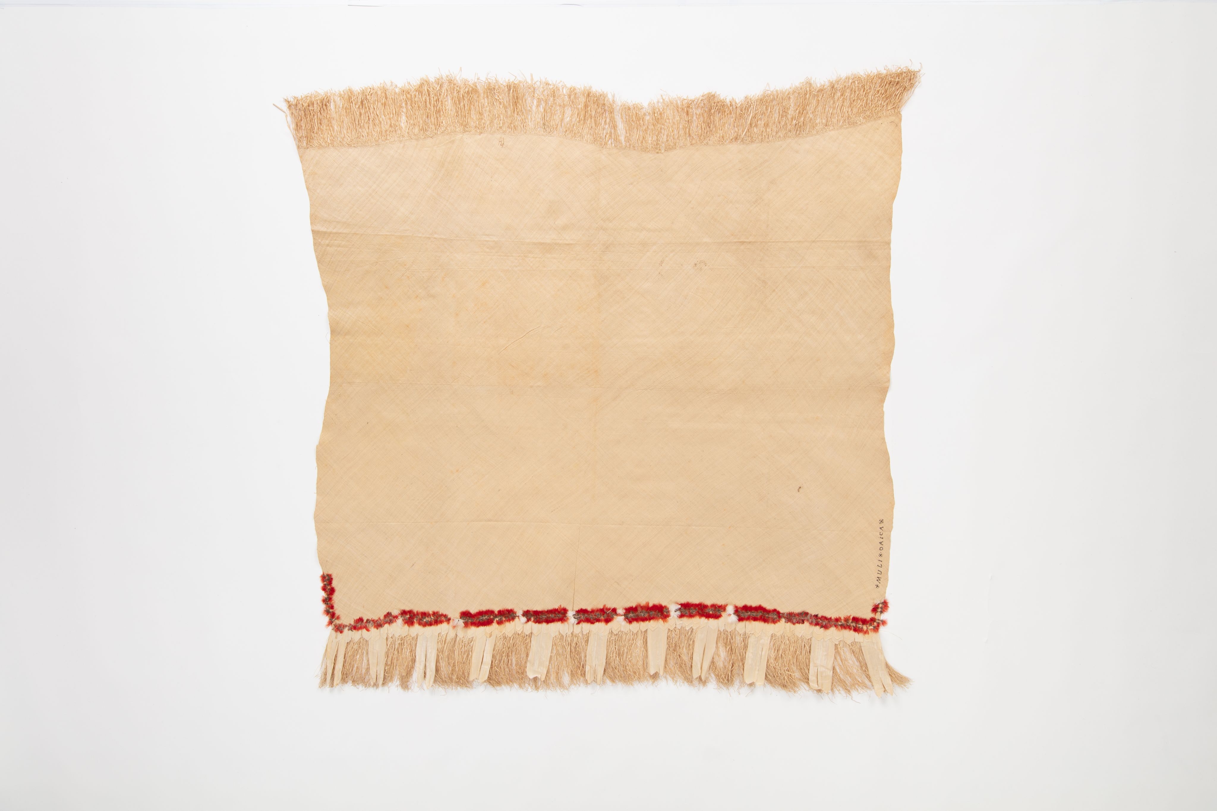 Fine mat made from pandanus (leaf) with "X MULI X OAIGA X" written the edge in ink. Red feathers are featured along the border of mat.