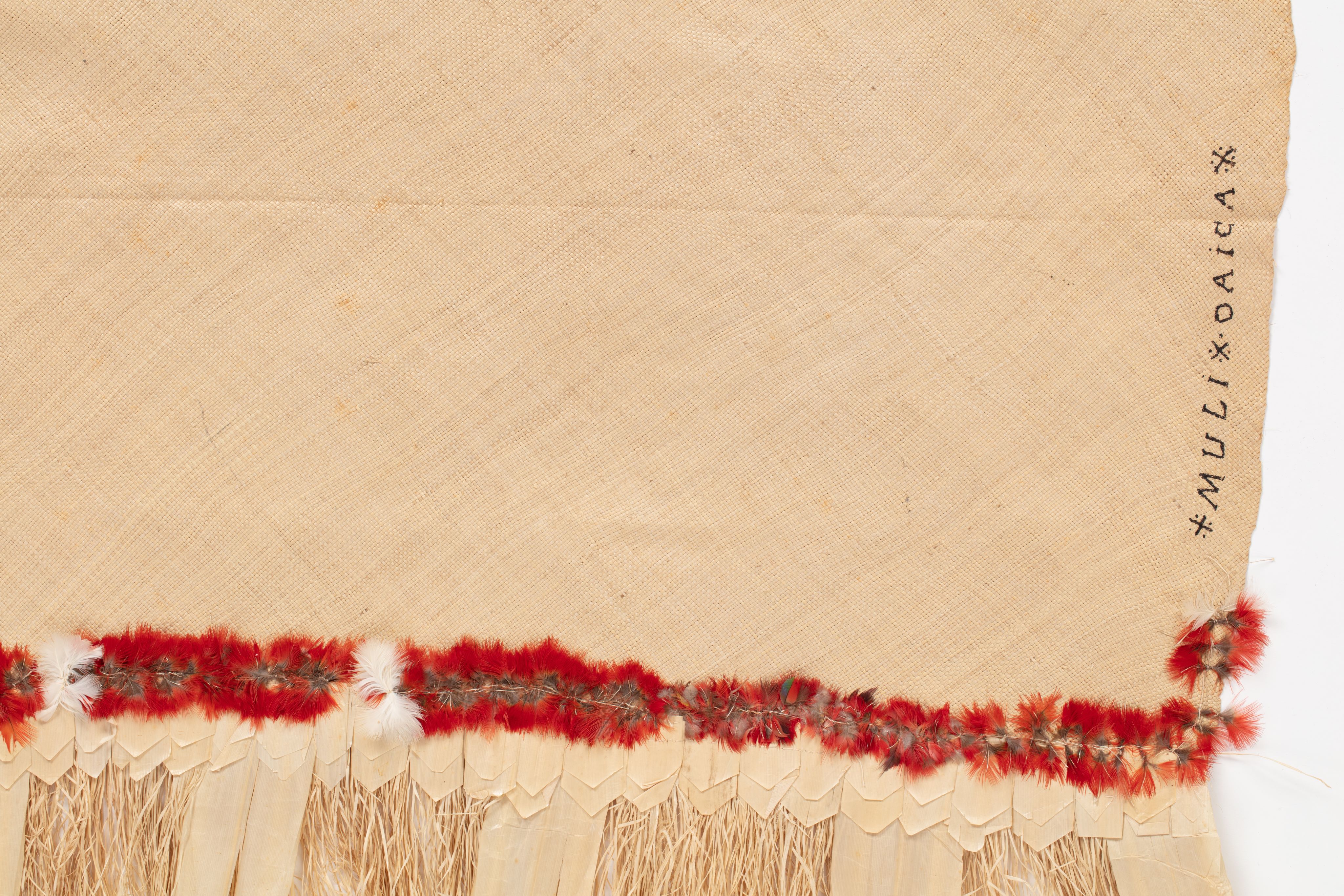 Fine mat made from pandanus (leaf) with "X MULI X OAIGA X" written the edge in ink. Red feathers are featured along the border of mat.