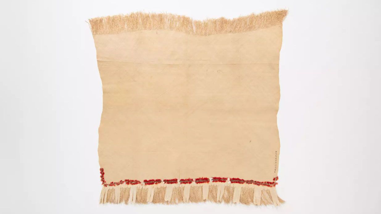 Fine mat made from pandanus (leaf) with "X MULI X OAIGA X" written the edge in ink. Red feathers are featured along the border of mat.