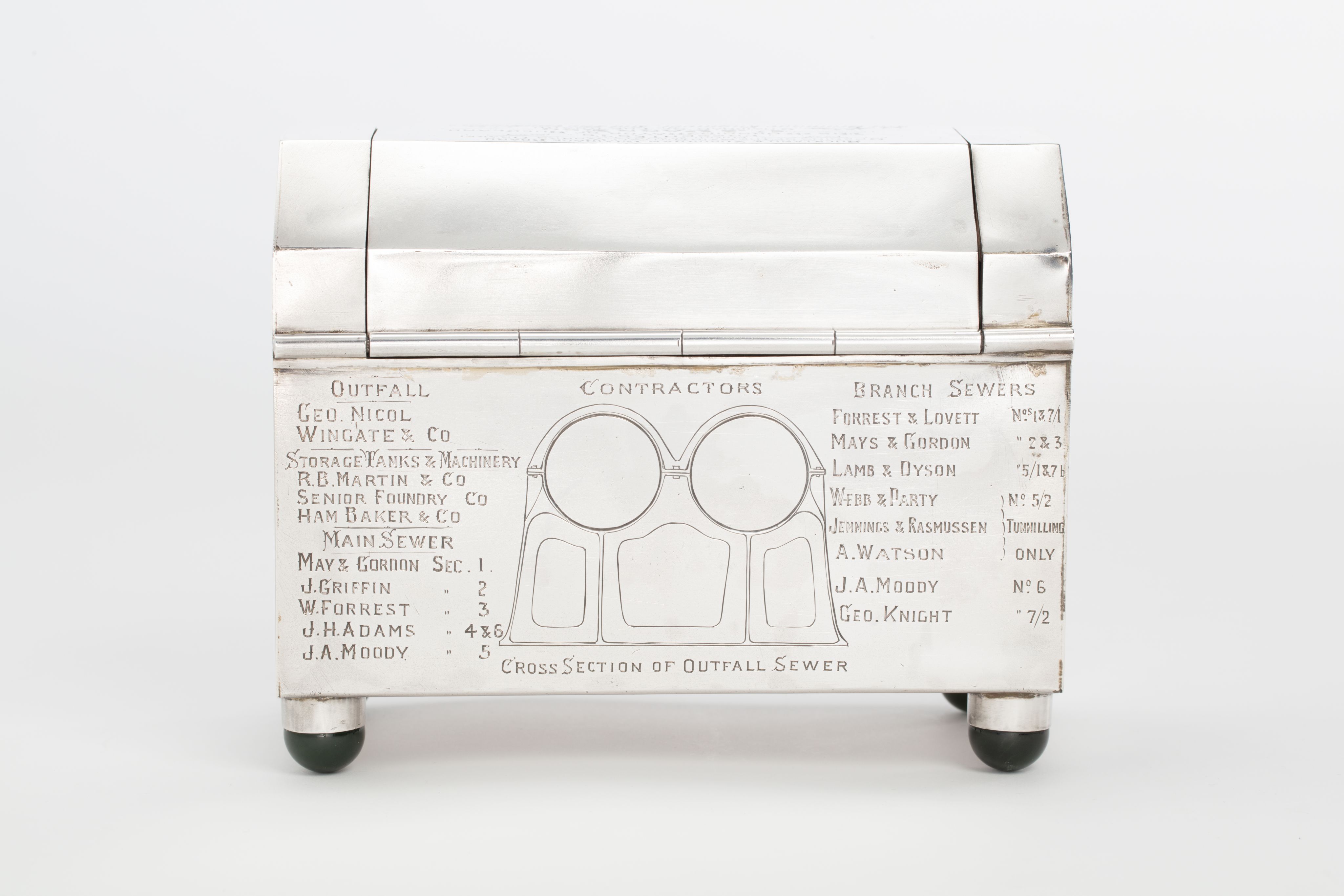 Finely crafted silver box (or casket) designed in the shape of the main sewage pipe, engraved with the names of the members of the drainage board along with technical sewage . On one side there is an engraved illustration of Ōkahu Bay, showing the Ngāti Whātua Ōrākei papakāinga and the newly installed sewer pipe running along the foreshore in front of it.