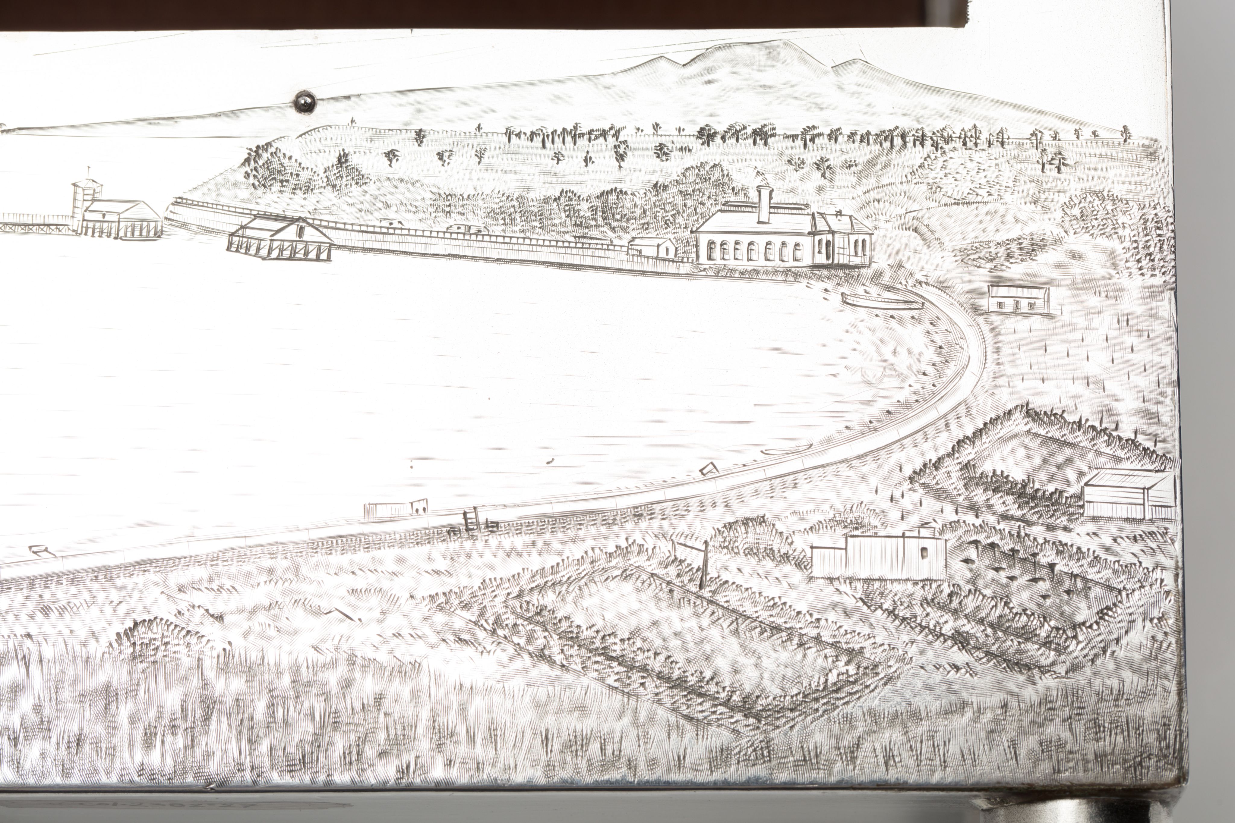 Finely crafted silver box (or casket) designed in the shape of the main sewage pipe, engraved with the names of the members of the drainage board along with technical sewage . On one side there is an engraved illustration of Ōkahu Bay, showing the Ngāti Whātua Ōrākei papakāinga and the newly installed sewer pipe running along the foreshore in front of it.