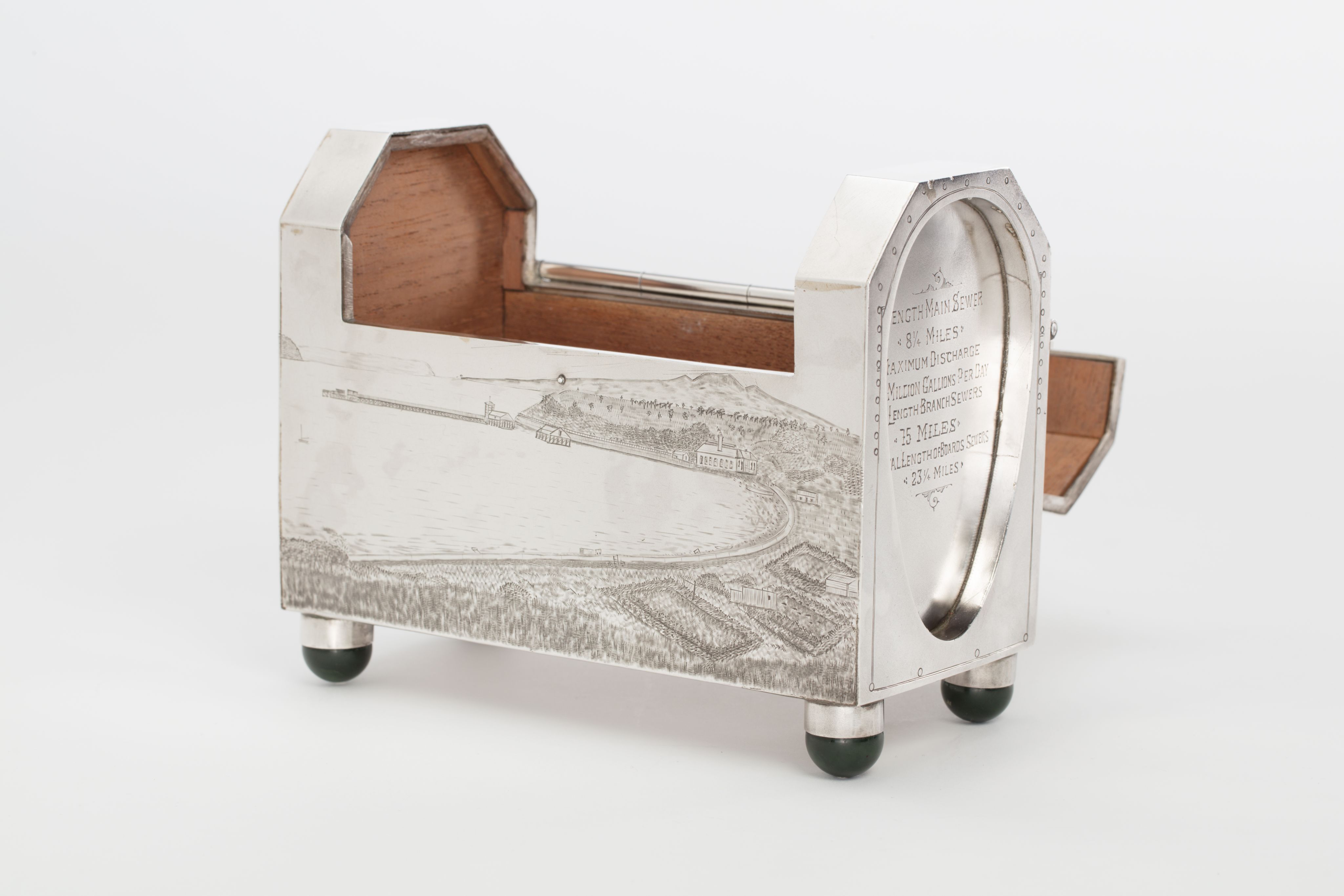 Finely crafted silver box (or casket) designed in the shape of the main sewage pipe, engraved with the names of the members of the drainage board along with technical sewage . On one side there is an engraved illustration of Ōkahu Bay, showing the Ngāti Whātua Ōrākei papakāinga and the newly installed sewer pipe running along the foreshore in front of it.