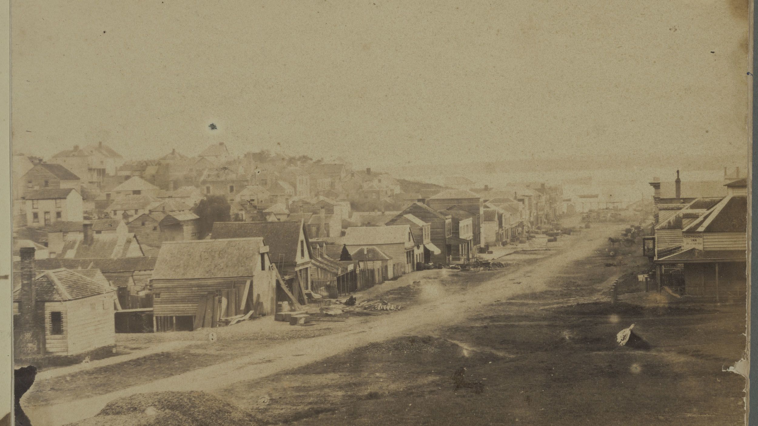 The image shows a sepia-toned monochrome photo of a city street with a number of houses on either side.  