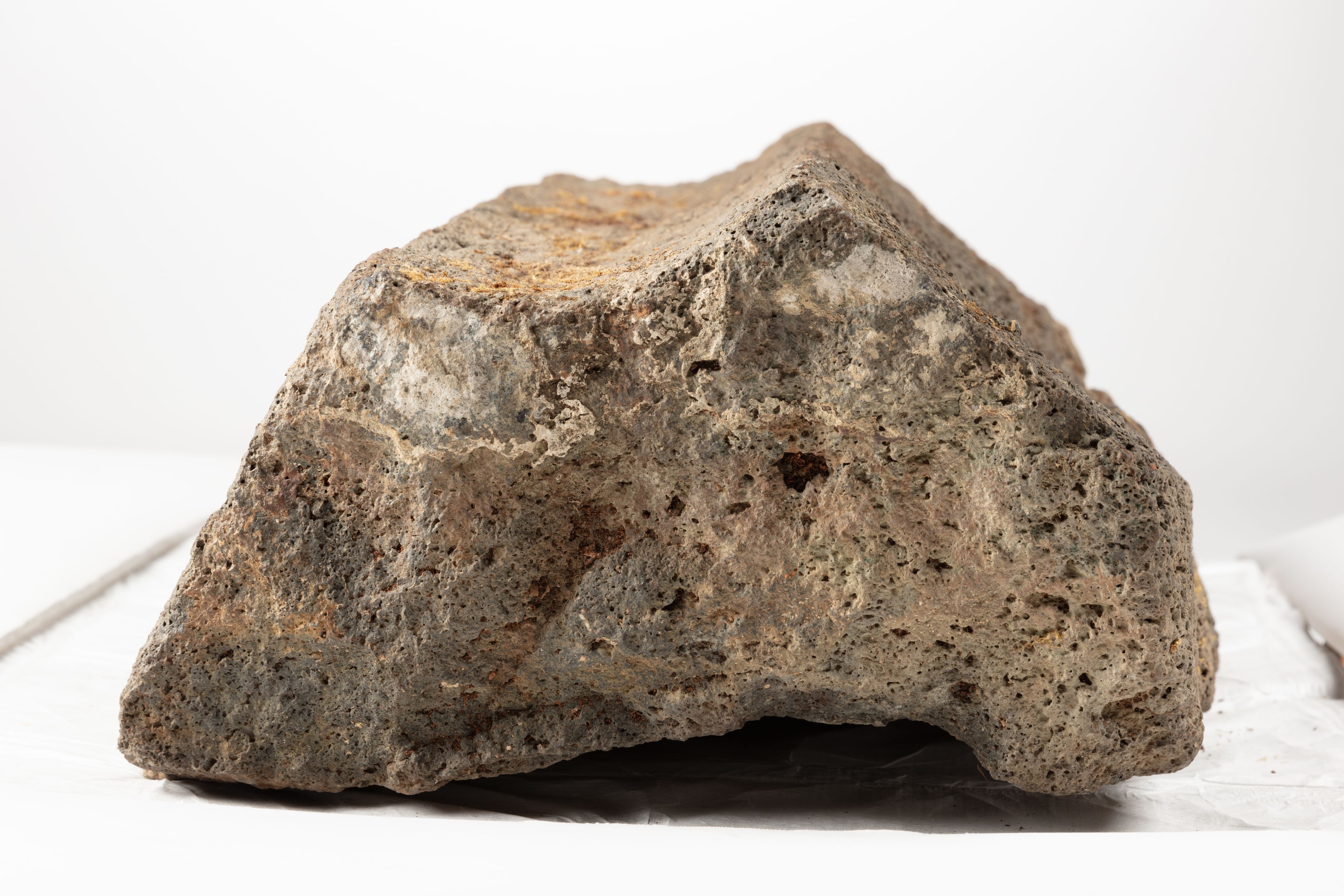 The image shows a large rock sitting atop a white surface. The rock is a mix of brown and grey colors, and the background is a bright white
