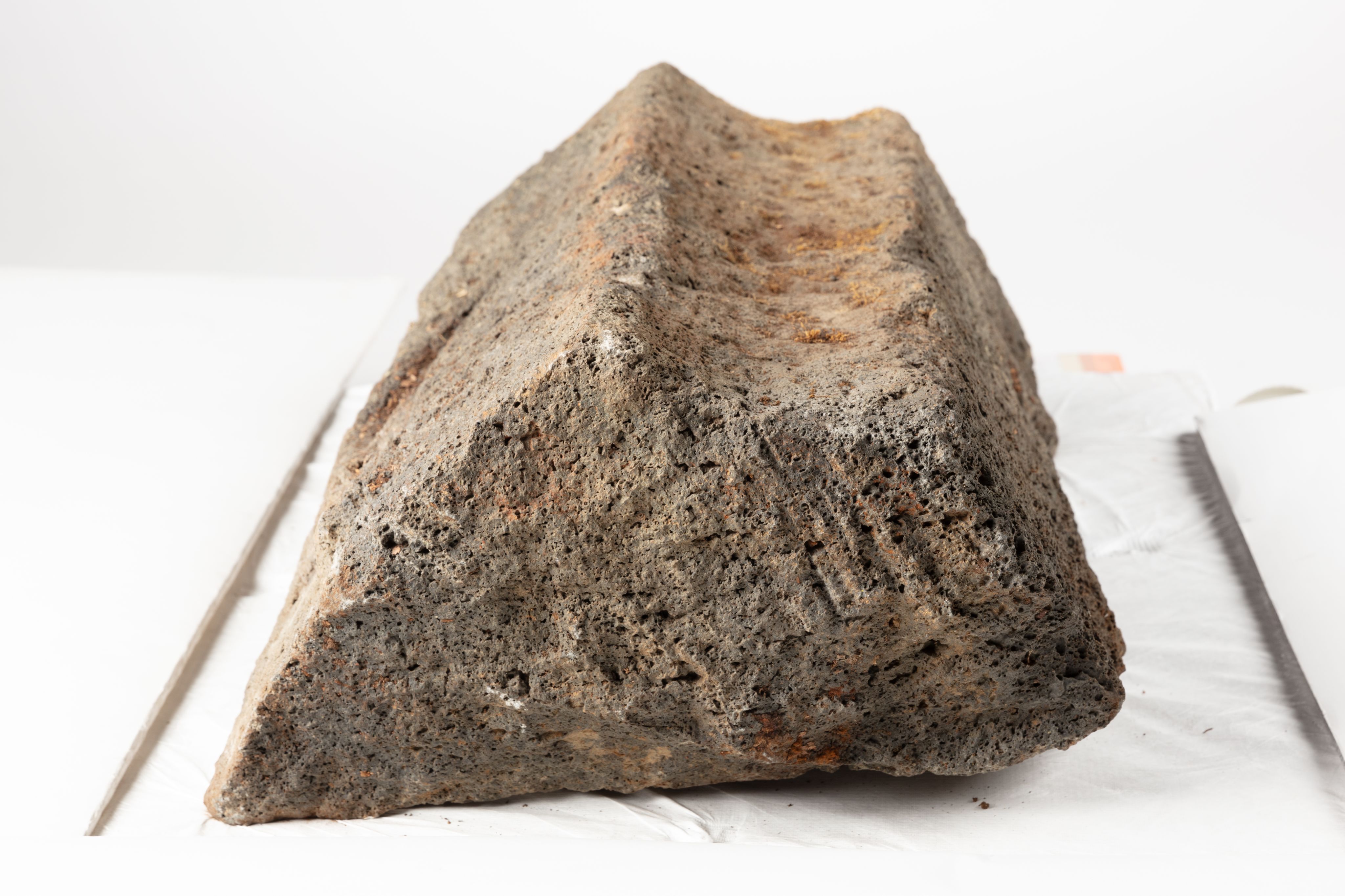 The image shows a large rock sitting atop a white surface. The rock is a mix of brown and grey colors, and the background is a bright white.